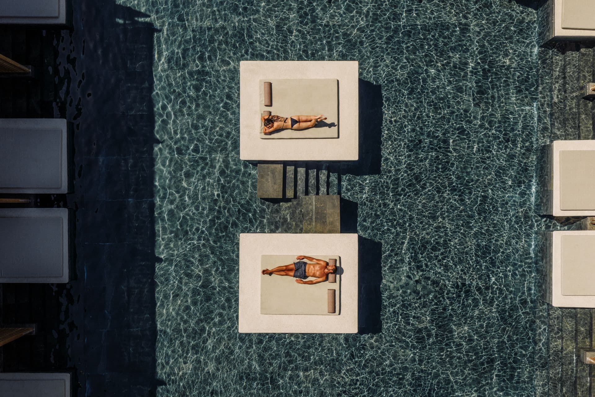 Alt text: Couple relaxing on sun loungers in a pool at one of the best resorts in Corfu for couples